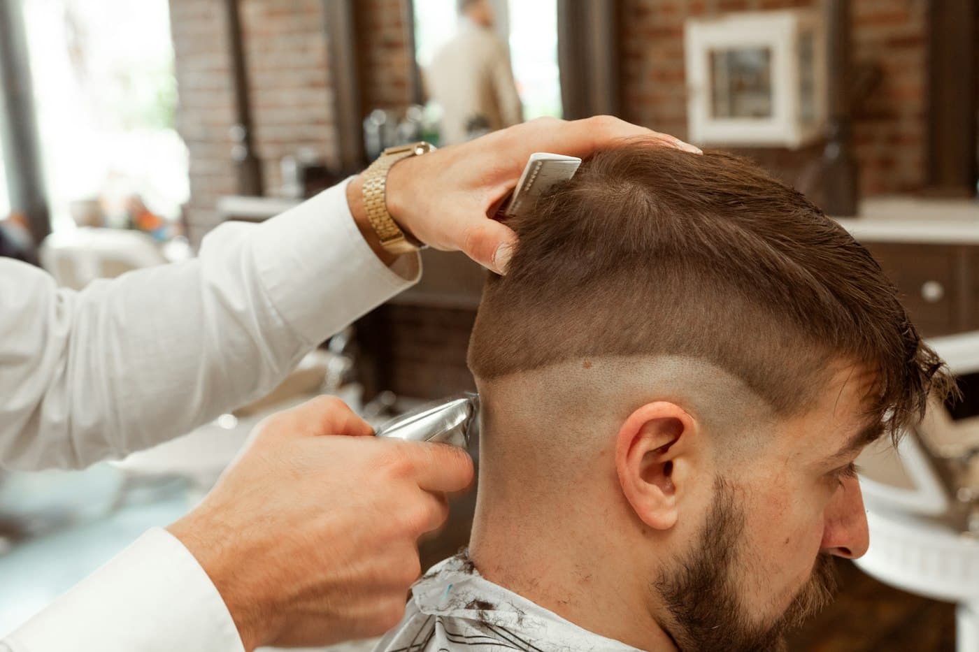 Barbeiro finalizando um corte degradê com máquina e pente