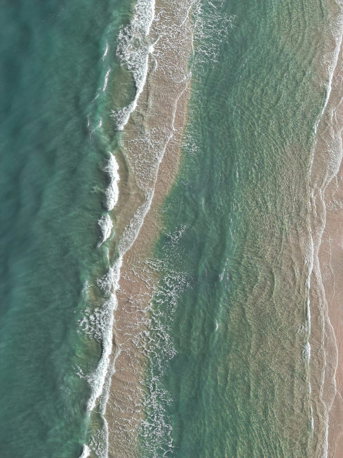 Vista aérea de ondas verdes chegando a uma praia de areia clara