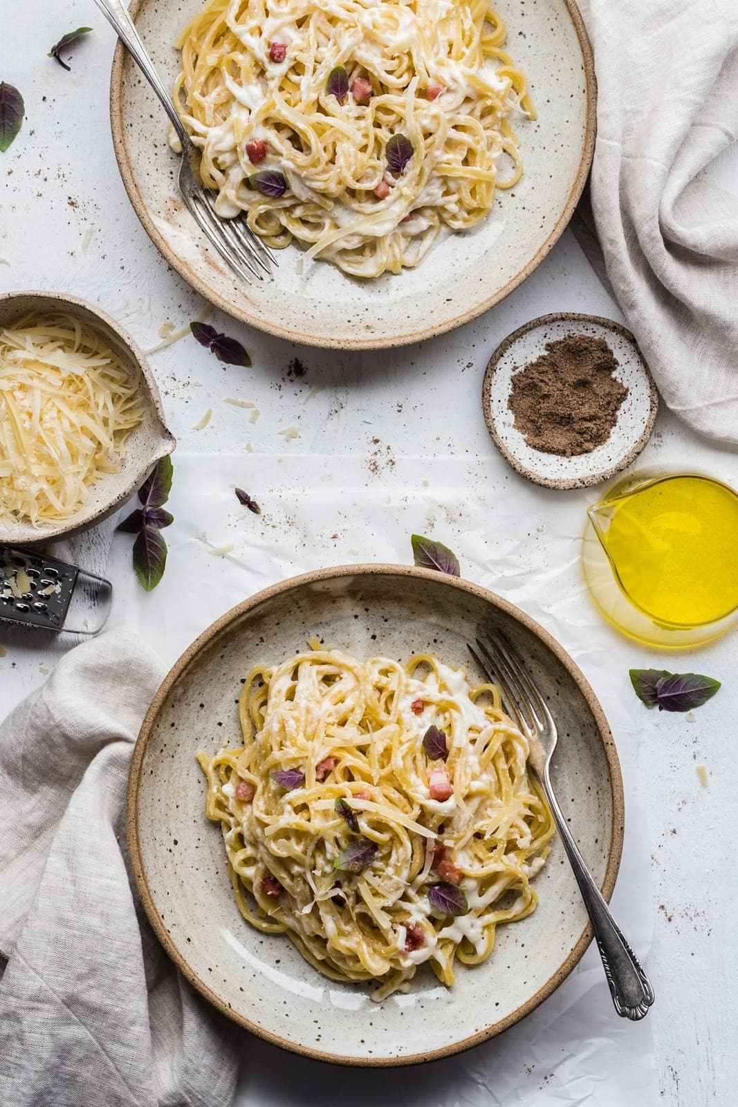 Massa à carbonara em pratos de cerâmica, com azeite e ingredientes à mesa